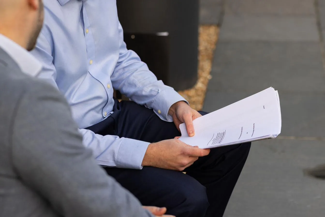 Two people seated outdoors turning the pages of a printed conservation covenant agreement.