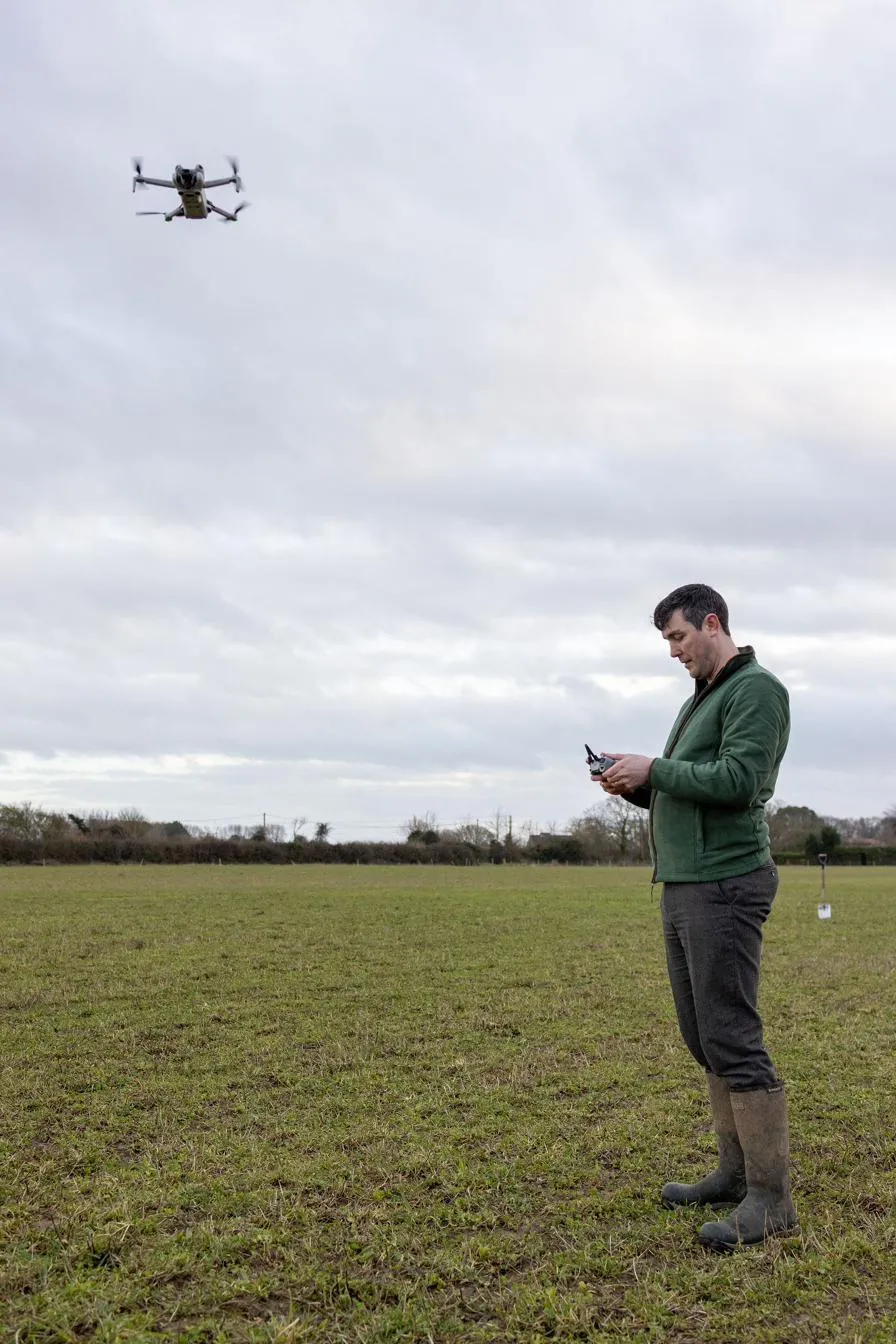 An ecologist flying a survey drone over open pasture, controller in hand.